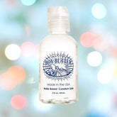 A small, clear bottle of Boy Butter "Clear" Water-Based Lubricant is set against a backdrop of blurred, colorful lights. The label emphasizes that it's "Made in the USA" and highlights its condom-safe, water-based cream formula. It's conveniently packaged in a 2 fl. oz. / 60 mL size.